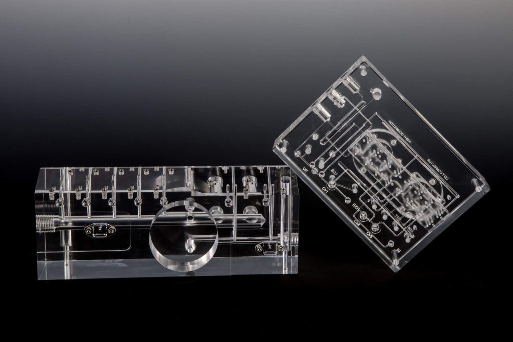 Precision Machined Acrylic Manifold Next to a Clear Diffusion Bonded Acrylic Fluidic Manifold